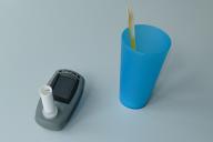 Medizinisches Atemmessgerät mit Mundstück neben einem blauen Kunststoffbecher mit einem gelben Löffel auf hellem Untergrund.