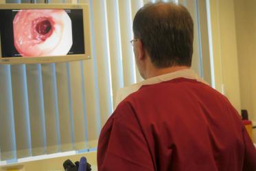 Arzt in roter Schutzkleidung betrachtet auf einem Monitor das Livebild einer Endoskopieuntersuchung mit Sicht auf den inneren Darmtrakt.