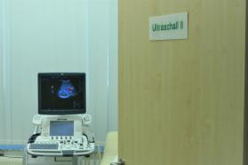Blick in einen Raum mit der Aufschrift „Ultraschall II“ auf der Tür, in dem ein Ultraschallgerät mit farblicher Darstellung auf dem Monitor steht.