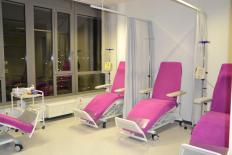 Heller Behandlungsraum mit mehreren pinkfarbenen Infusionsstühlen, Infusionsständern und Vorhängen zur Abtrennung der Bereiche